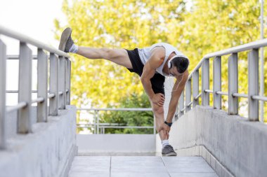 Genç erkek koşucu sporcu eğitim ve egzersiz açık havada şehirde yapıyor. Egzersiz yaparken müzik dinliyor