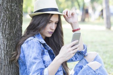  Genç güzel kadın onun akıllı üzerinde seyir şapka ile açık havada telefon ve güzel da tadını çıkarın