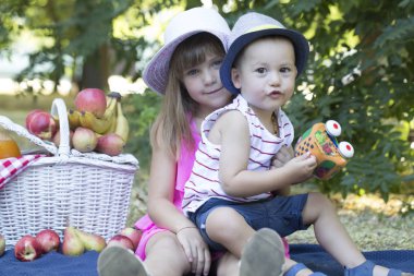  küçük sevimli erkek ve kız üzerinde bir battaniyeye çimlere oturup oynamak. Kız çocuk sarıldı. Erkek ve kız bir piknik sepeti meyve suyu ve meyve sürü vardır. Kız ve erkek kardeş arasında aşk