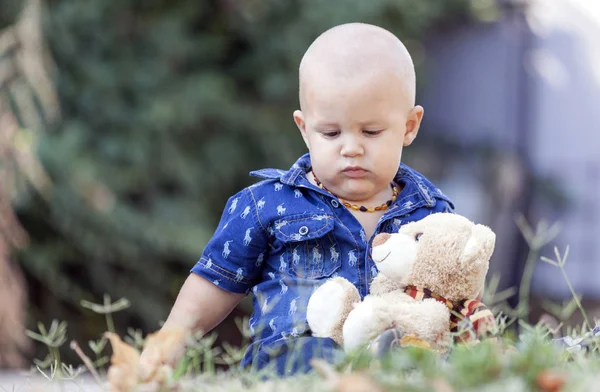 一个可爱的小男孩在夏天坐在草地上玩他最喜欢的填充玩具时的肖像 — 图库照片
