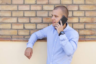 Bir cep telefonu konuşurken yakışıklı bir genç adam dışında portresi. Arkasında bir duvar eski tuğla var. Kopya alanı