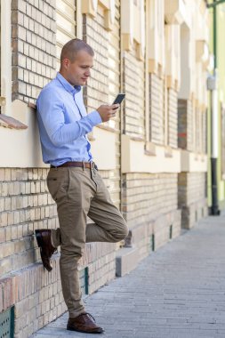 Bir cep telefonu kullanırken yakışıklı bir genç adam dışında portresi. Eski bina yanında duruyor. Manifatura mesaj. Kopya alanı