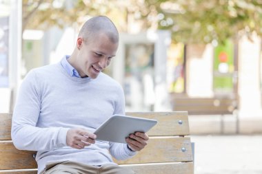 Şehir ve kullanır dijital tablet bir bankta oturan adam, öğrenci, gülümseyen yakışıklı genç
