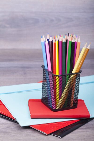 School and office supplies on a wooden background. On the table there are wooden crayons of different colors, notes and folders. Copy space