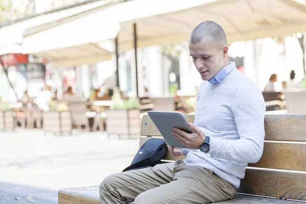 Entrepreneur working texting in a digital tablet sitting on a bench in th city. He uses a tablet for work and for everyday life