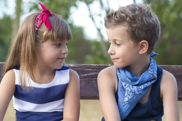 小可爱的男孩和一个女孩坐在公园的长凳上 玩得很开心 他们看着对方的眼睛 — 图库照片
