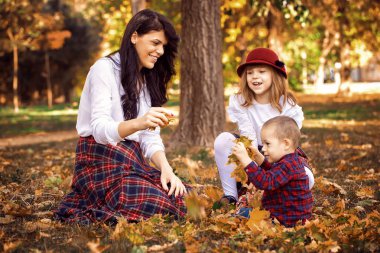 Güzel genç anne parkta çocuklarını sonbaharda çalış. Onlar kuru düşen yapraklar ile oynarken iyi vakit geçiriyor musun.