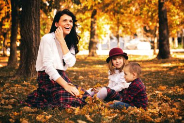 Güzel genç anne parkta çocuklarını sonbaharda oynamaya. Onlar kuru düşen yapraklar ile oynarken iyi vakit geçiriyor musun. Seçici odak ve küçük alan derinliği