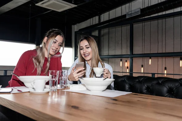 Female Friends Having Lunch Together At The Restaurant. Two young women using a mobile phone during lunch