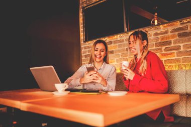 Restoran modern bir iç tasarıma kahve içme ve seyir telefon iki genç modern kızlar. Dostluk ve teknoloji. Seçici odak ve küçük alan derinliği