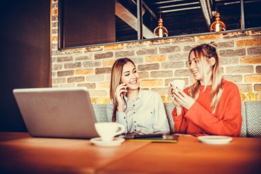 Restoran modern bir iç tasarıma kahve içme ve akıllı telefon kullanarak iki genç güzel kız. Dostluk ve teknoloji. Seçici odak ve küçük alan derinliği.