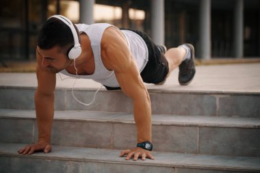Sabah egzersiz açık havada için hazırlanıyor erkek koşucu egzersiz, yukarı itin yapıyor. Germe Egzersiz yaparken, kulaklık aracılığıyla müzik dinlediği