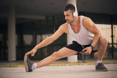 Eğitim parkta hazırlanıyor genç sporcu germe egzersiz yapmak. Egzersiz yaparken, o heasphones üzerinden müzik dinler. Fitness, spor, yaşam kavramı