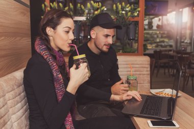 Mutlu genç çift ya da bir dizüstü bilgisayar kullanarak, limonata içmek ve kafede otururken gülümseyen arkadaşlar