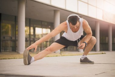 Eğitim parkta hazırlanıyor genç sporcu germe egzersiz yapmak. Egzersiz yaparken, o heasphones üzerinden müzik dinler. Fitness, spor, yaşam kavramı