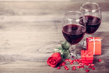 İki kadeh kırmızı şarap, gül ve hediye ile dekorasyon ahşap masa üzerinde kırmızı kalpler tarafından. Sevgililer günü kutlama kavramı. Kopya alanı.