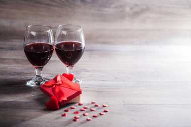 İki kadeh kırmızı şarap, hediye kutusu ve ahşap masa üzerinde kırmızı kalpler. Sevgililer günü kutlama kavramı. Kopya alanı.