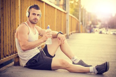 Genç adam içme suyu süre oturan, kulaklık ile müzik dinlemek ve eğitimden sonra dinlenme bir şişe portresi.