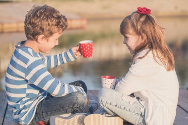 Kız ve erkek sahilde günbatımı anda oynamak. İlk aşkım. Mutlu çocuklar çay içme ve keyfi yerinde göl keyfi. 