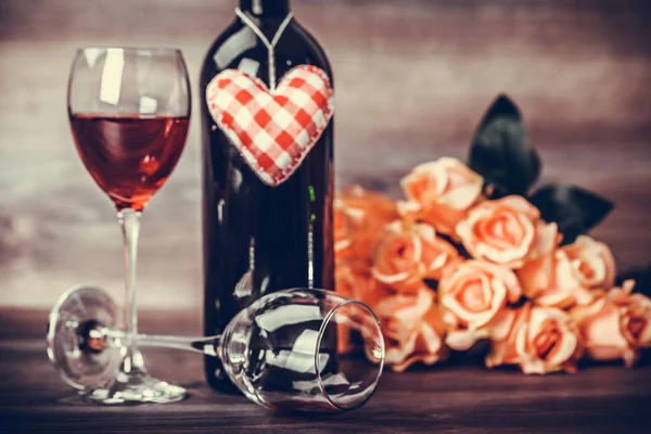 Red wine bottle, two glasses of wine, roses with decoration by red hearts on wooden table. Valentines day celebration concept. Copy space.