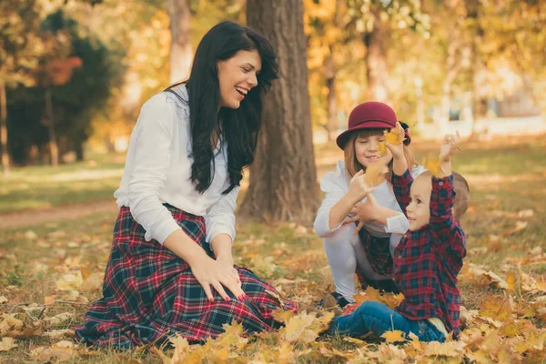 娘と秋に公園で一緒に遊ぶ幼い息子の笑みを浮かべてください 彼らは乾いた落ち葉で遊んで良い時間を過ごしています 幸せな家族 — ストック写真