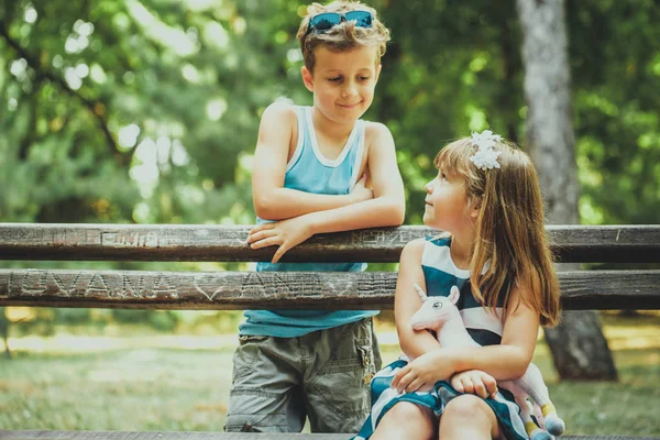 小可爱的男孩和快乐的女孩坐在公园的长凳上 玩得很开心 他们看着对方的眼睛 — 图库照片