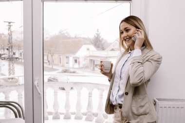 Kahve molası. Ofiste ayakta ve telefon görüşmesi genç gülümseyen bir işkadını. İş, eğitim, yaşam tarzı kavramı