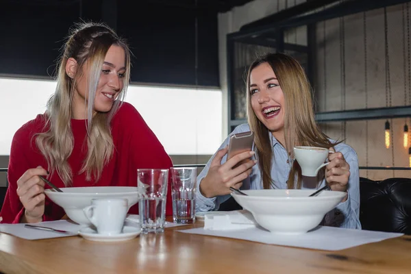 Female Friends Having Lunch Together At The Restaurant. Two young women using a mobile phone during lunch