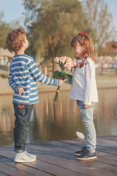 日落时 女孩和男孩在海滩上玩耍 快乐的孩子们享受湖 同时有一个美好的时光 男孩给了一个女孩一束美丽的鲜花 — 图库照片