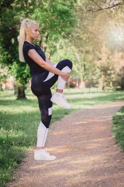 Germe yapmak çekici sportif kız parkta bacaklar için egzersizler. Giymiş spor giyim.