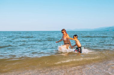 Anne ve oğlu deniz kıyı çalışıyor. Onlar el ele tutuşarak.