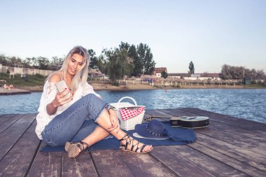 Ahşap iskele, Smartphone cep telefonu ile mesaj üzerinde oturan güzel gülümseyen kadın. Seyahat ve tatil. Özgürlük kavramı