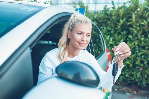 Driving school. Young happy woman sitting in a car. Driver sutdent proudly showing the key. Free space for text. Copy space.