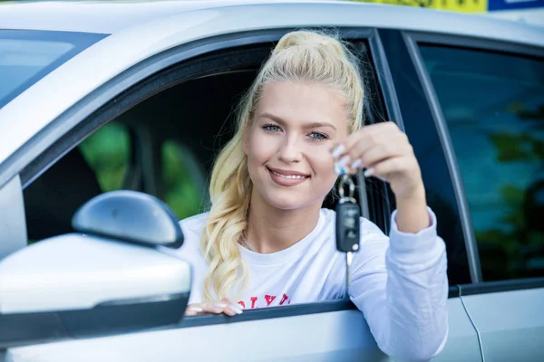 Driving school. Young happy woman sitting in a car. Driver sutdent proudly showing the key. Free space for text. Copy space.