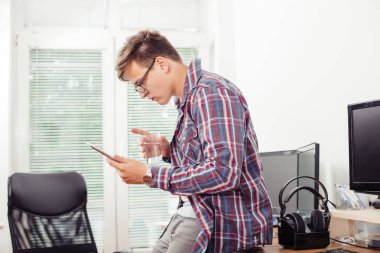 Kendine güvenen genç adam onun ofisinde oturan ve bir bardak su tutan dijital tablet üzerinde çalışan yan görünüm.