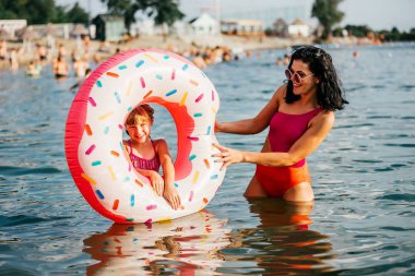 Anne ve kızı suda ıslatın ve şişme çörek eğleniyor. Yaz tatili