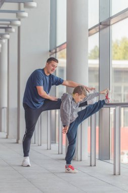 Küçük bir çocuk ve onun eğitmeni germe bacak egzersizleri, birlikte bir spor merkezinde yaptığı. Baba ve oğul birlikte vakit ve sağlıklı bir yaşam tarzı yol. Birlikte çalışma dışarı. Fitness gün. 