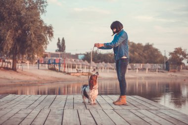 Elini tutarak ve köpeğini Basset Hound nehrin yanında oynamaktan genç kadın yan görünüm