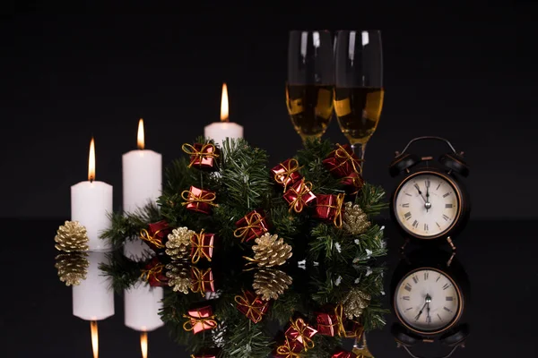 Two wine glasses with champagne, clock, candle and Christmas ornaments on a black background with reflection. Copy space. Merry Christmas and Happy New Year, background