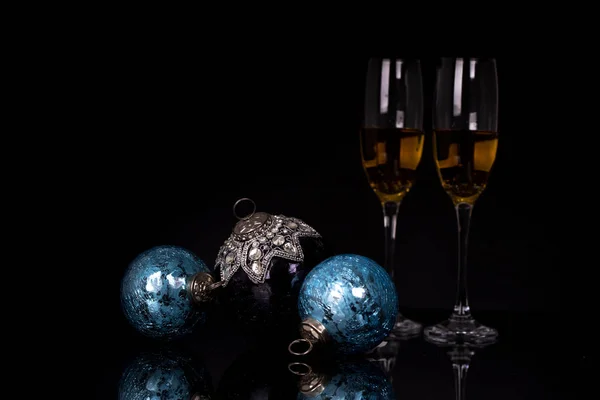 Two wine glasses with champagne, clock and Christmas ornaments on a black background with reflection. Copy space. Merry Christmas and Happy New Year, background