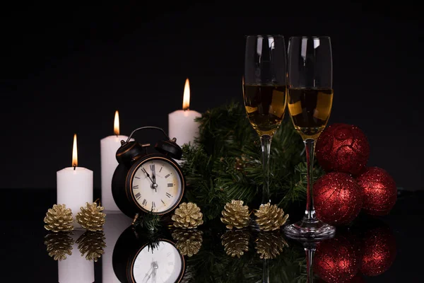 Two wine glasses with champagne, clock, candles and Christmas ornaments on a black background with reflection. Copy space. Merry Christmas and Happy New Year, background