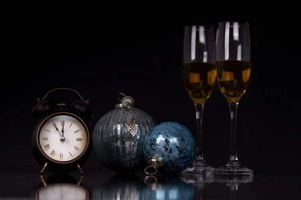Two wine glasses with champagne, clock and Christmas ornaments on a black background with reflection. Copy space. Merry Christmas and Happy New Year, background