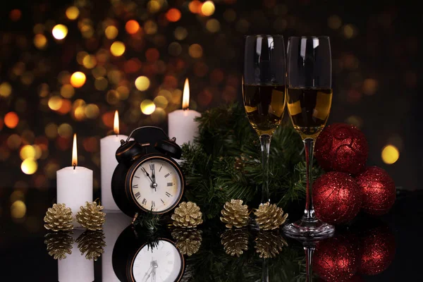 Two wine glasses with champagne, clock, candles and Christmas ornaments on a black background with reflection. Copy space. Merry Christmas and Happy New Year, background