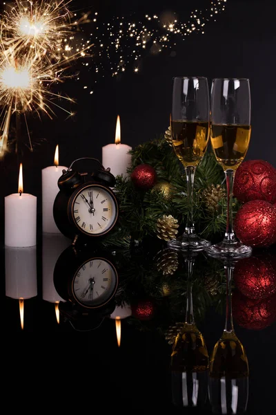 Two wine glasses with champagne, clock, candles and Christmas ornaments on a black background with reflection. Copy space. Merry Christmas and Happy New Year, background