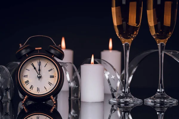 Two wine glasses with champagne, clock and candles on a black background with reflection. Copy space. Merry Christmas and Happy New Year, background