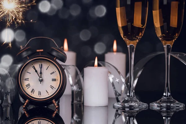 Two wine glasses with champagne, clock, sparklers and candles on a black background with reflection. Copy space. Merry Christmas and Happy New Year, background