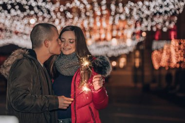 Genç mutlu çift havai fişekleri ile kış şehir gece eğleniyor. Genç adam öper ve onun kız arkadaşı sarılarak