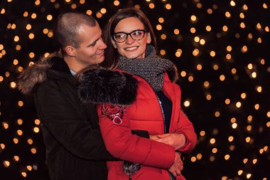 Attractive couple in love hugging, looking at each other and enjoying an intimate moment together, against the backdrop of city lights - Image