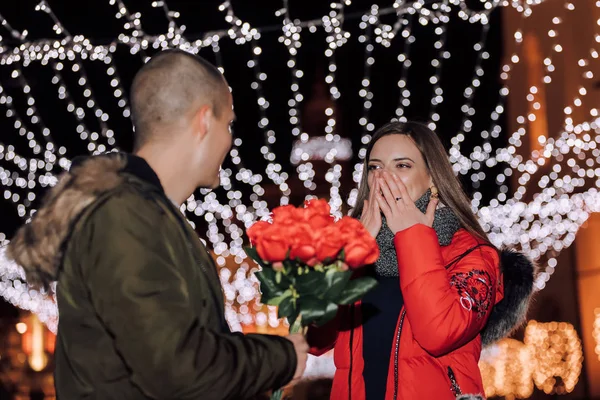 Valentine\'s day or anniversary concept - Handsome man is giving his girlfriend bouquet of roses at night in the city street