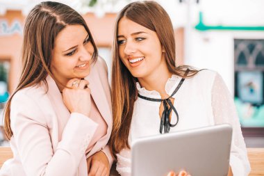 İki güzel genç gülümseyen bir bankta oturan ve tablet vasıl arayan kadın